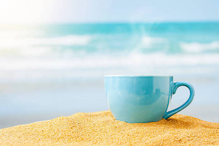 blue cup of coffee on white sand beach